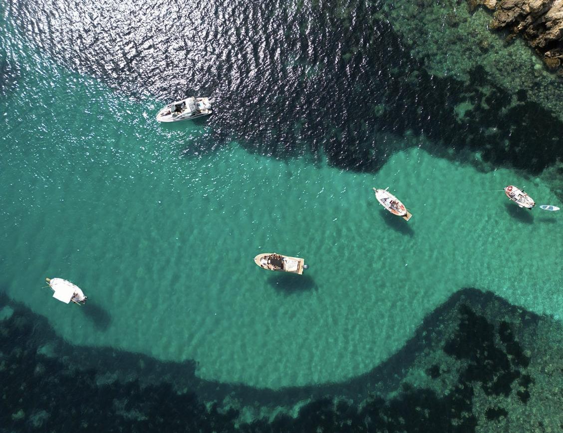 Vista cenital de una cala con aguas cristalinas y barcos fondeados