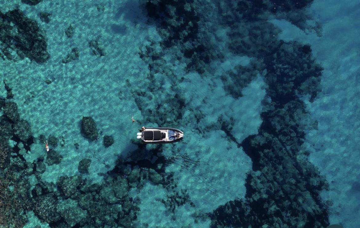 Semirrígida fondeada sobre fondo rocoso con personas haciendo snorkel